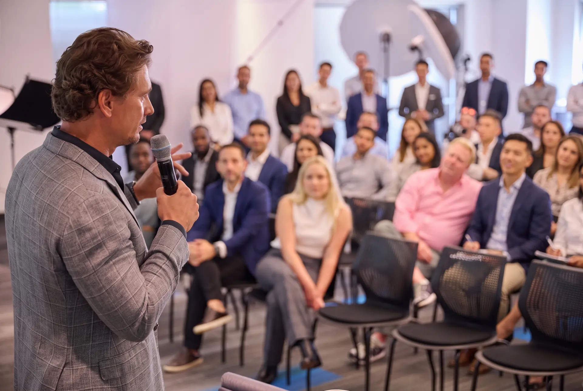 Speaker holding a microphone in front of a seated audience of professionals at a corporate event