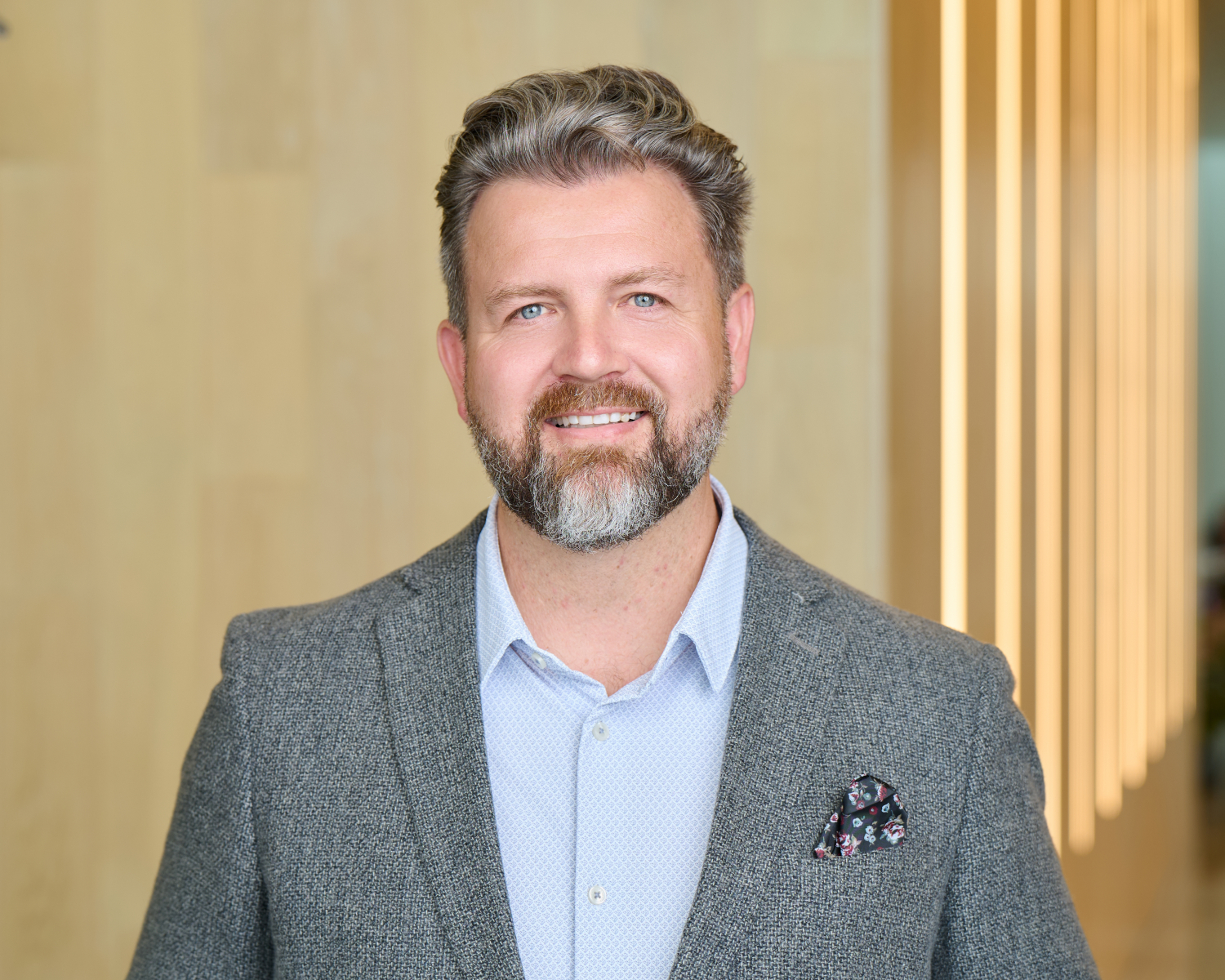 Corporate headshot of a smiling professional man in a gray blazer