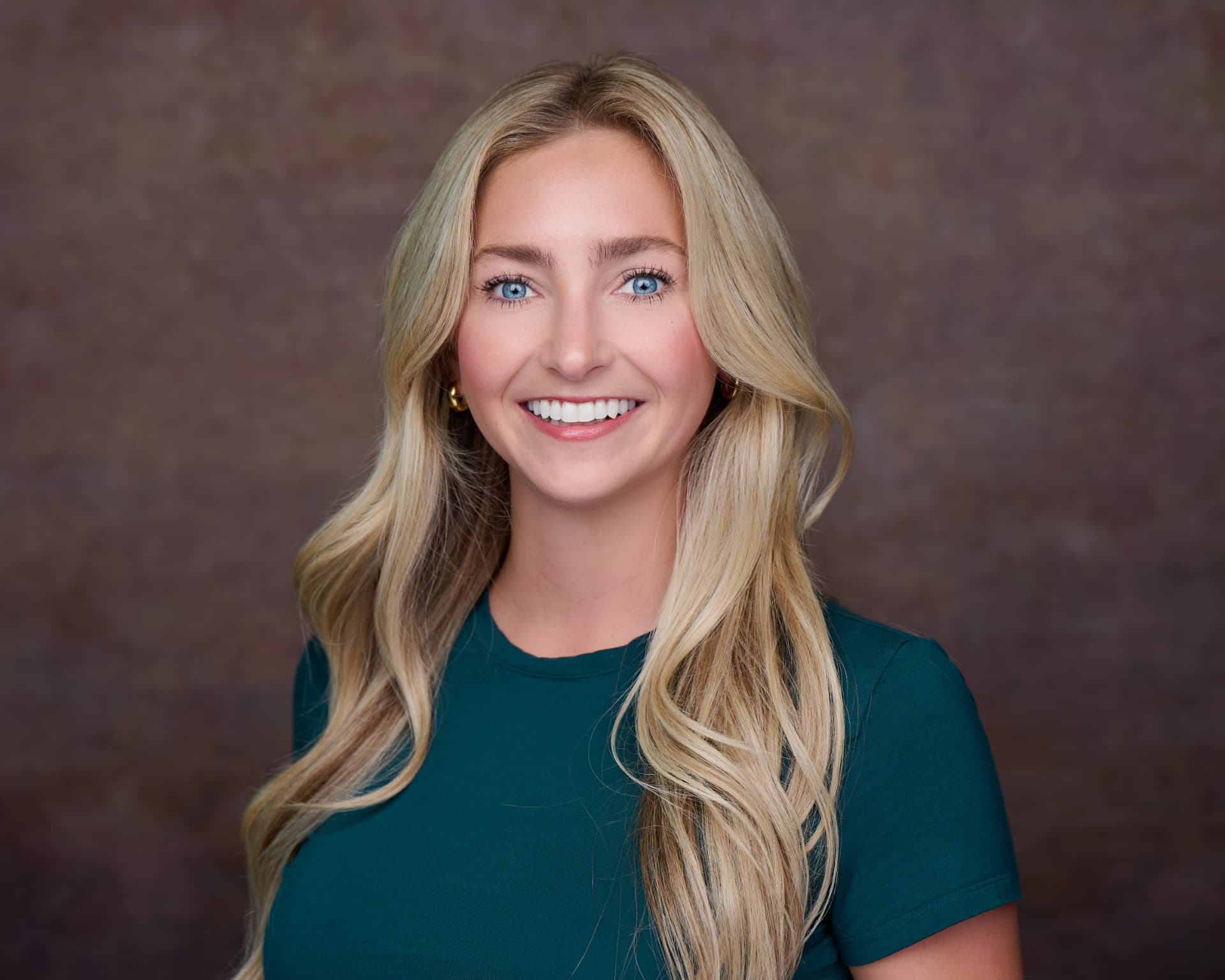 Professional headshot of a smiling woman in a dark green shirt against a warm brown backdrop